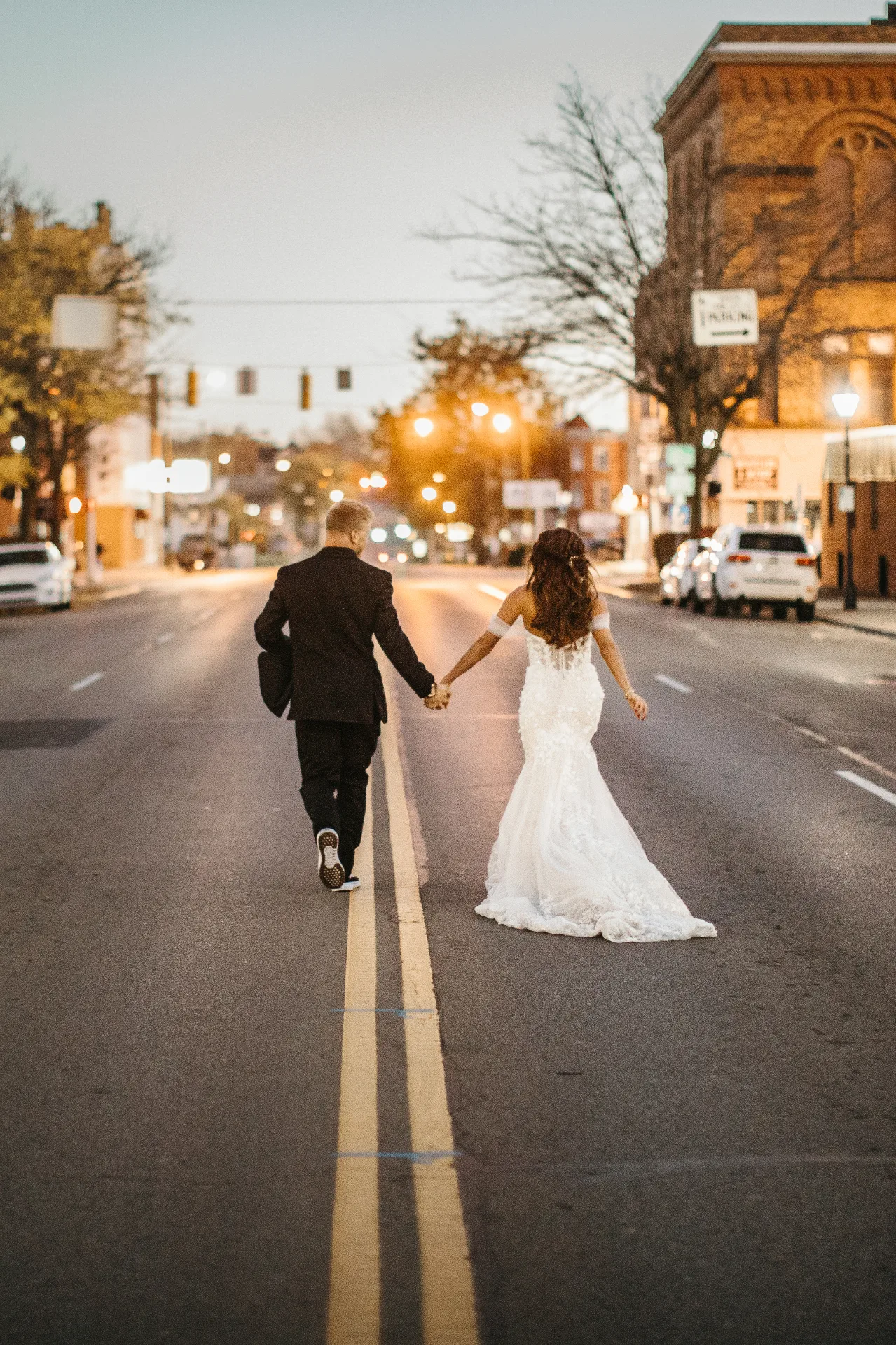 Bride and groom walking hand in hand down a Marion street at golden hour