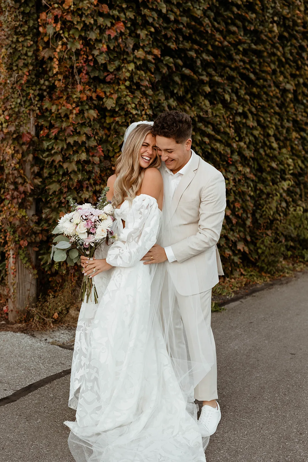 Bride and groom laughing by the ivy wall at Brickyard on Main