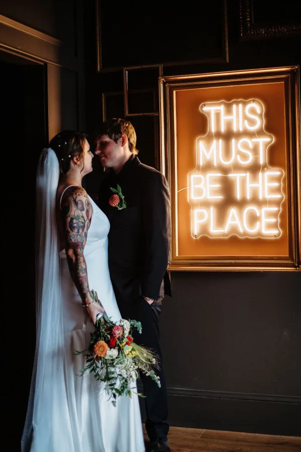 Bride and groom by the 'This Must Be The Place' neon sign at Urban501
