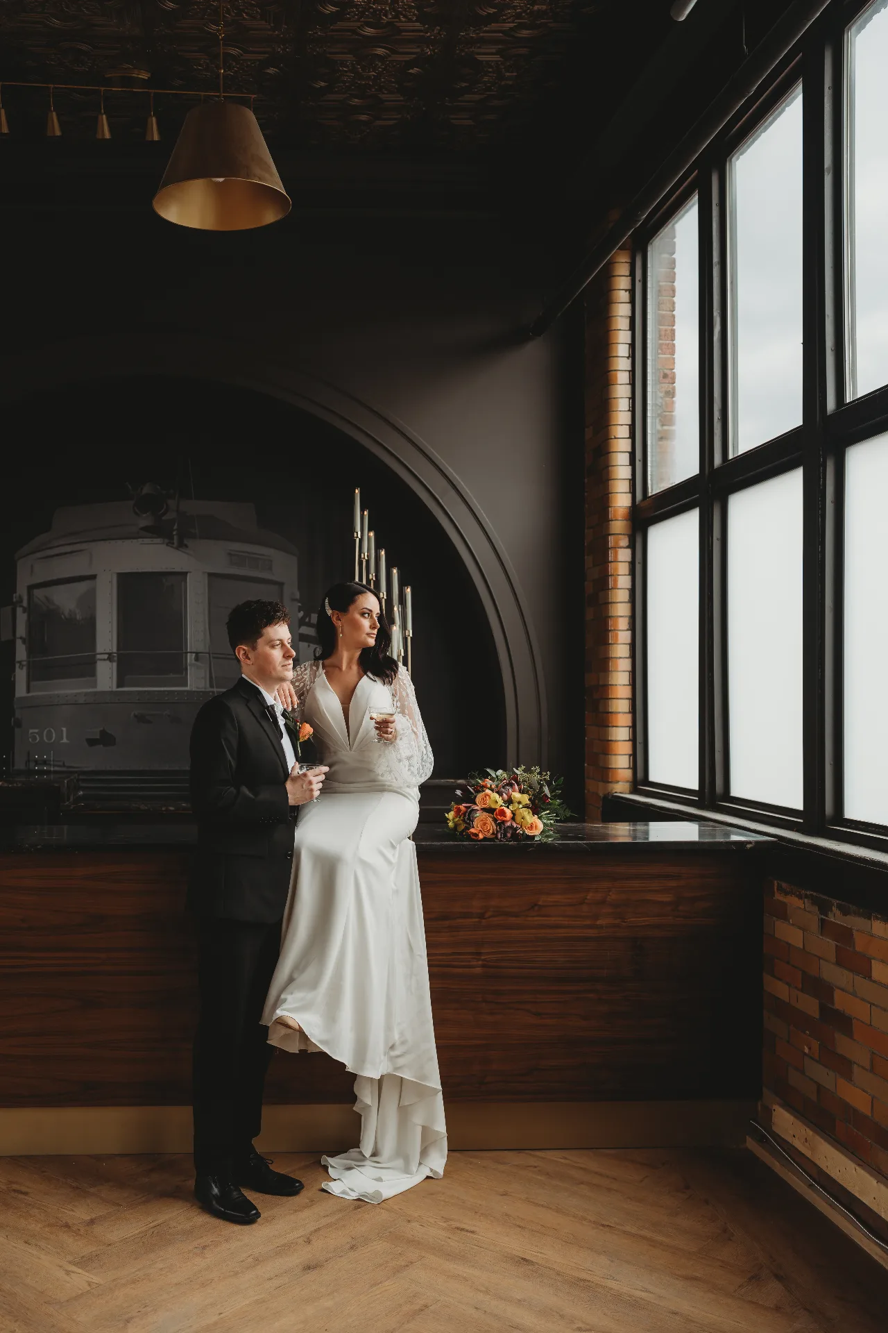 Couple with champagne by the arched window and 501 rail car mural at Urban501